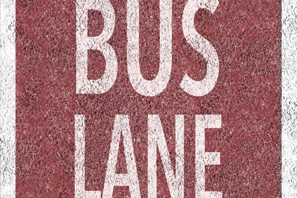 Overhead view of white BUS LANE sign painted on red background on concrete street.